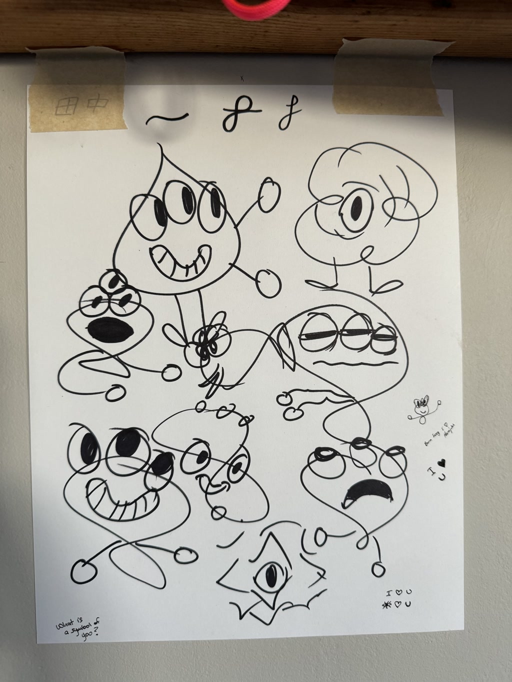 Various hand-drawn cartoon-like characters are sketched on a white paper. Each character uniquely expresses a range of emotions or states like happiness, surprise, and anger. They appear playful and whimsical, with exaggerated facial expressions. Some features are simplistic with large eyes and expressive mouths, while others have detailed aspects like eyeglasses or different hairstyles. The paper is casually taped to a surface at the top left and top right corners with what appears to be tan-colored tape.