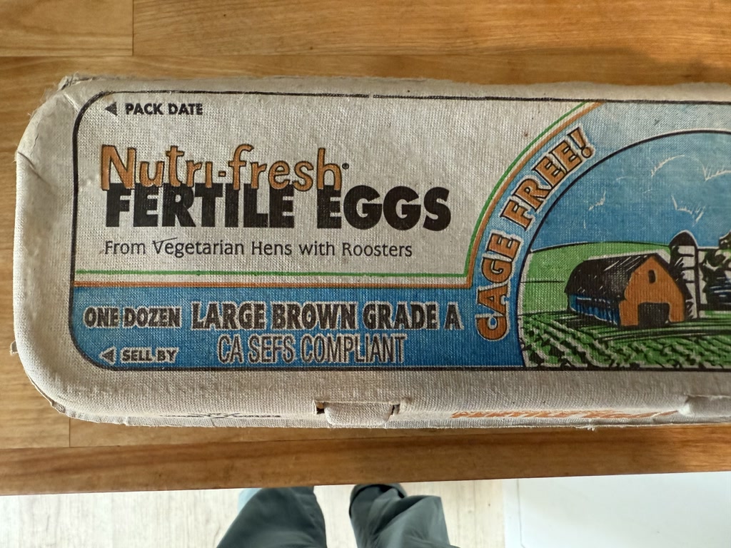 An egg carton labeled 'Nutri-fresh FERTILE EGGS' from vegetarian hens with roosters. It is cage-free and contains one dozen large brown Grade A eggs. The carton indicates it is CA SEFS compliant. The packaging features an illustration of a barn and fields.