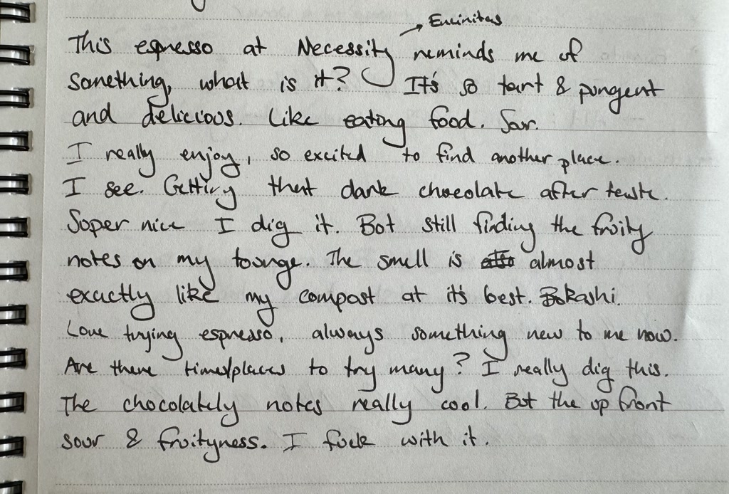 A page from a spiral notebook with handwritten notes. The notes capture someone's experience tasting an espresso at a location called 'Necessity.' The writer expresses enjoyment of the espresso, noting its tart and pungent qualities, as well as dark chocolate aftertaste and fruity notes. They compare the aroma to their compost at its best, using the word 'Bokashi,' a composting method. The person is intrigued by the combination of flavors, mentioning chocolatey notes combined with upfront sour and fruitiness, and seems open to trying espresso in different places.